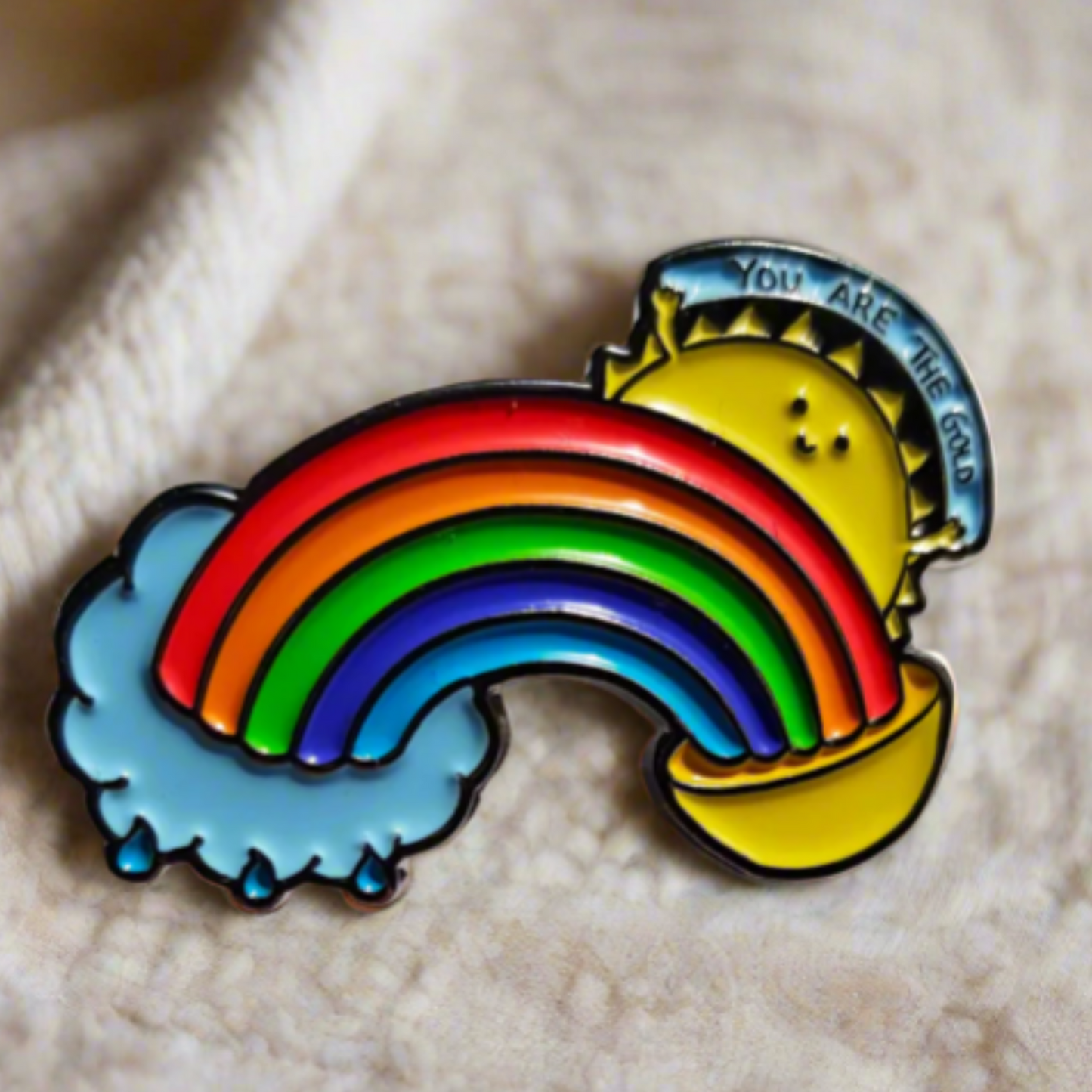 A ‘You Are the Gold’ enamel pin attached to a white sweater, showcasing its vibrant rainbow and sun design. A perfect self-care and mental wellness accessory.