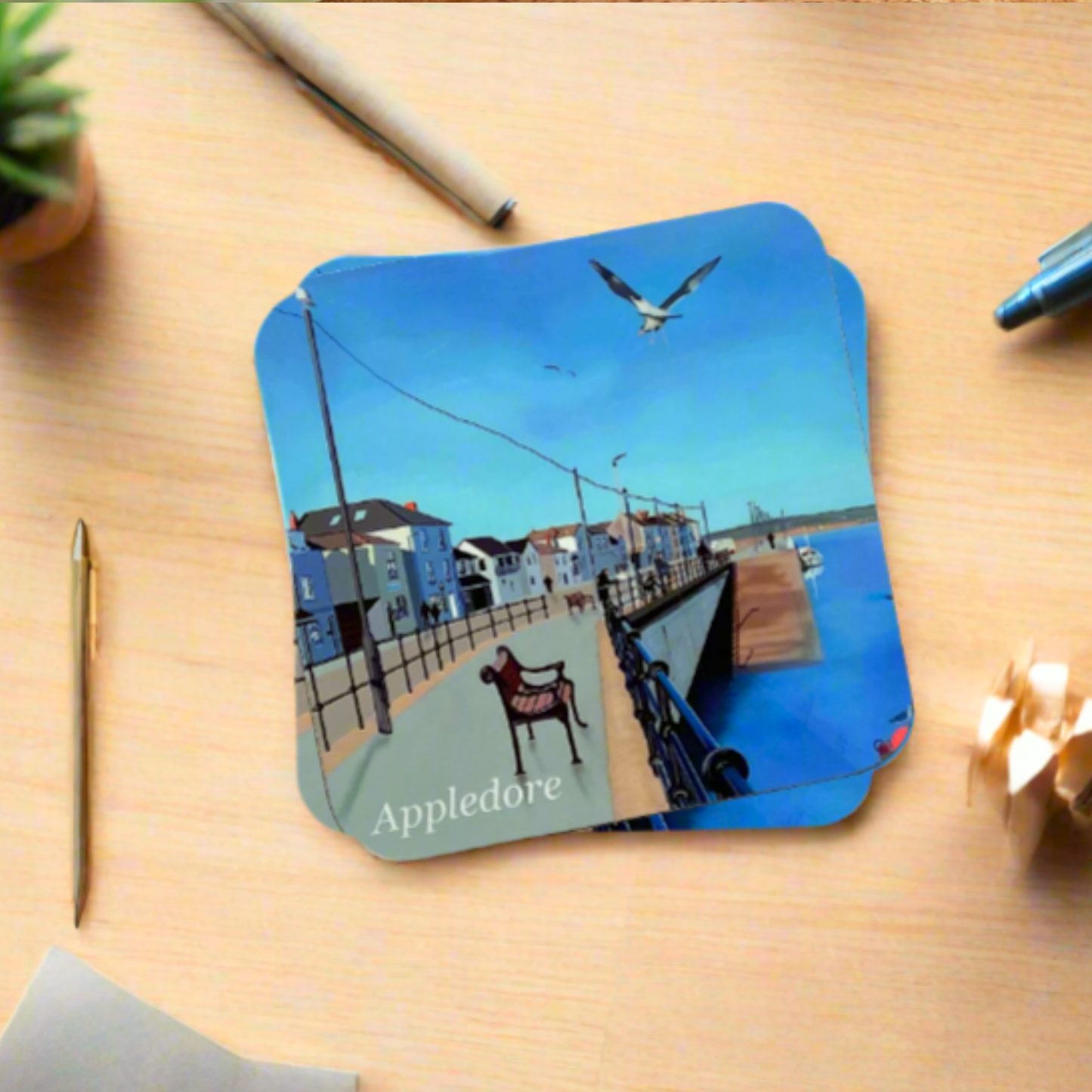 Appledore coaster by Jagos Art with the quayside, a bench, seagulls flying, blue sky and blue river water