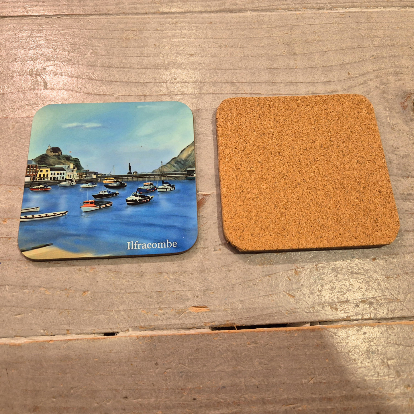 Ilfracombe coaster by Jagos Art with boats in the harbour, blue sea, harbour shops, blue sky and cork back