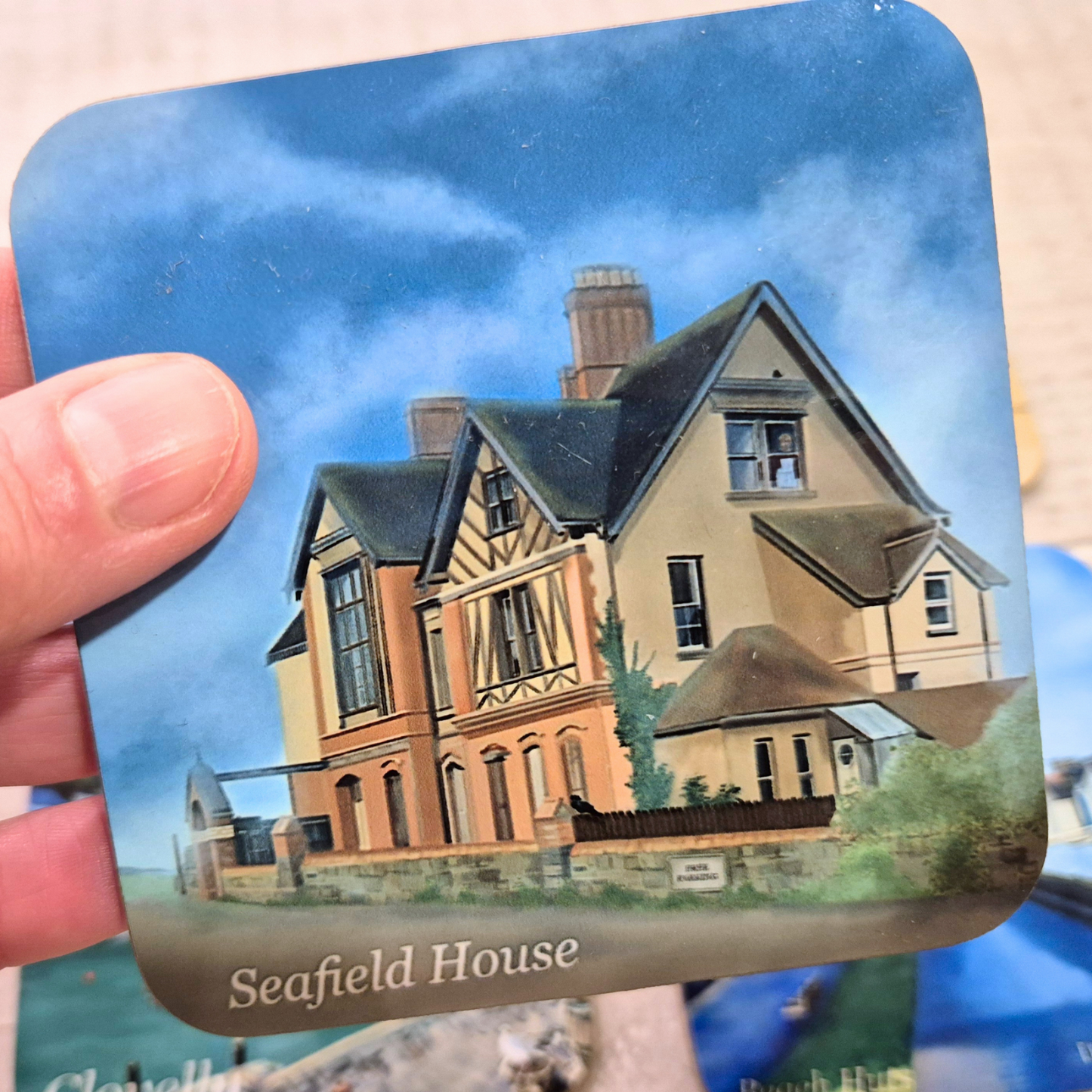 Seafield House coaster by Jagos Art with cloudy skies held in hand