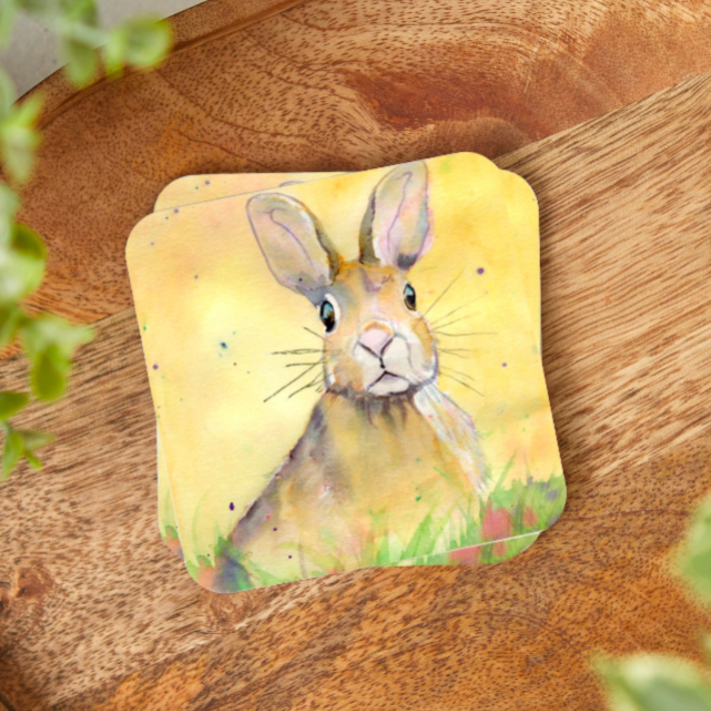 a coaster featuring a print of an original watercolour painting by artist Jagos Art of a startled yet cheeky looking hare sitting in the grass with a vibrant yellow background