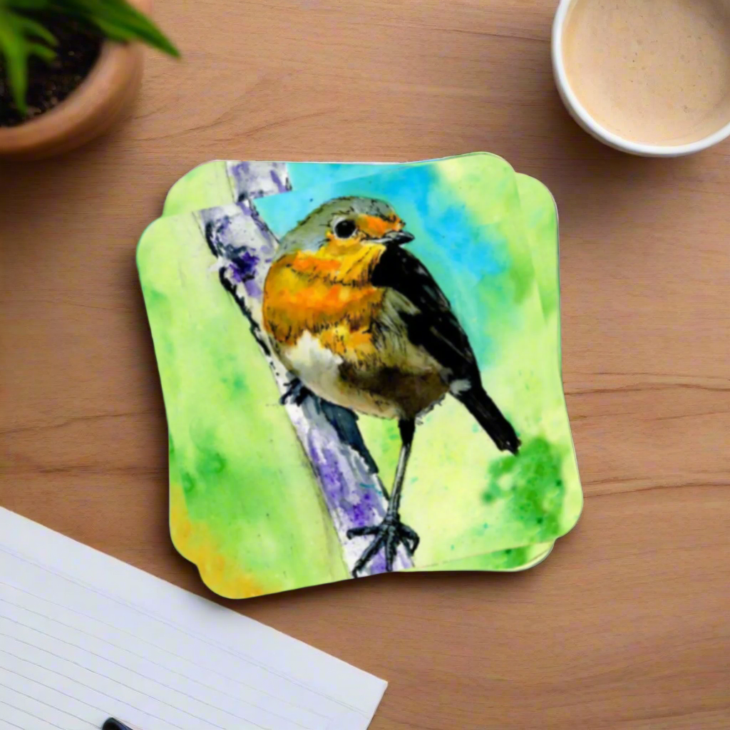a coaster featuring a print of an original watercolour painting of a robin, with a green blended background, sitting on a branch, on a table also showing a hint of a plant, a notepad and a cup of coffee
