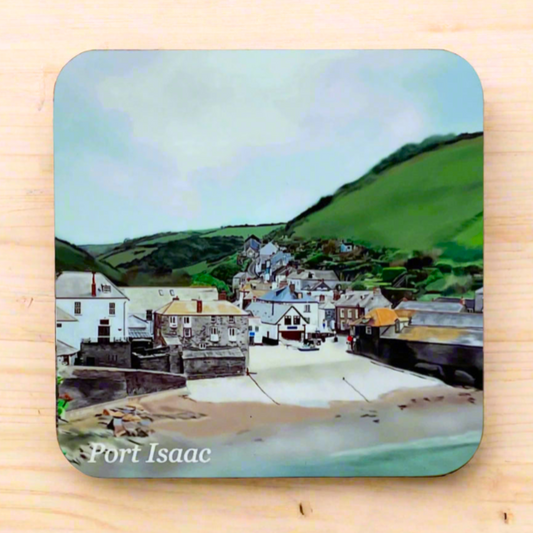 "A square glossy coaster on a desk, featuring a digital illustration of Port Isaac by artist Jagos Art. The artwork showcases harbour shops, the beach slipway, historic buildings, and scenic fields in the background. Printed using the sublimation process."
