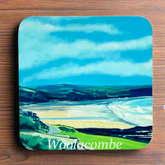 "A square glossy coaster on a desk, featuring a digital illustration of Woolacombe by artist Jagos Art. The artwork showcases the beach and the field landscape behind. Printed using the sublimation process
