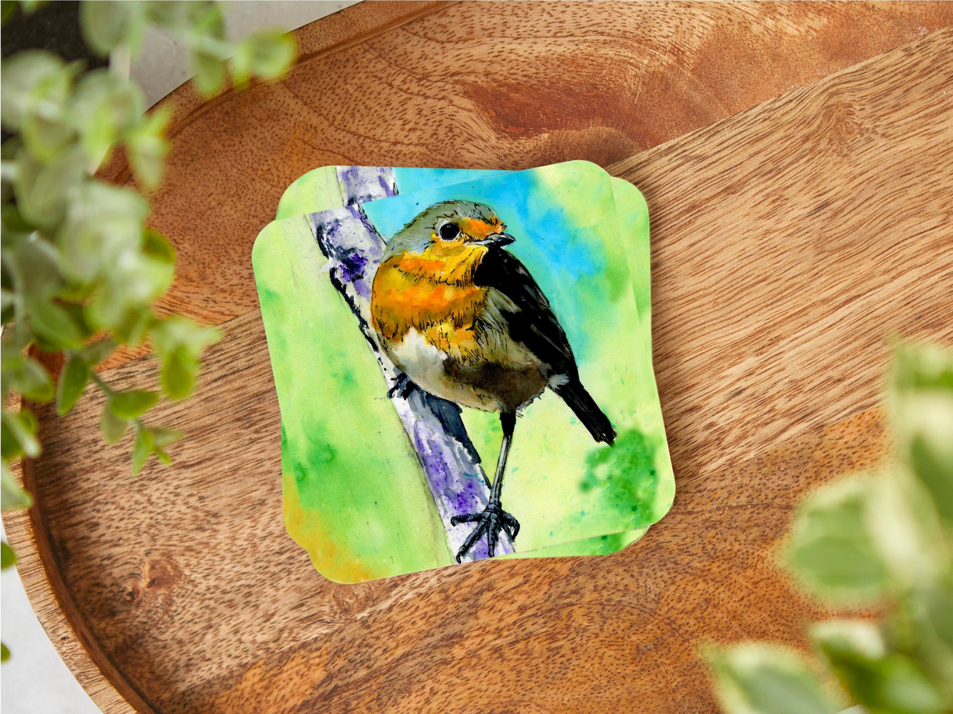 A coaster featuring a print of a vibrant art print of an original watercolour painting of a gorgeous Robin perched on a tree branch with a lovely green and blue background