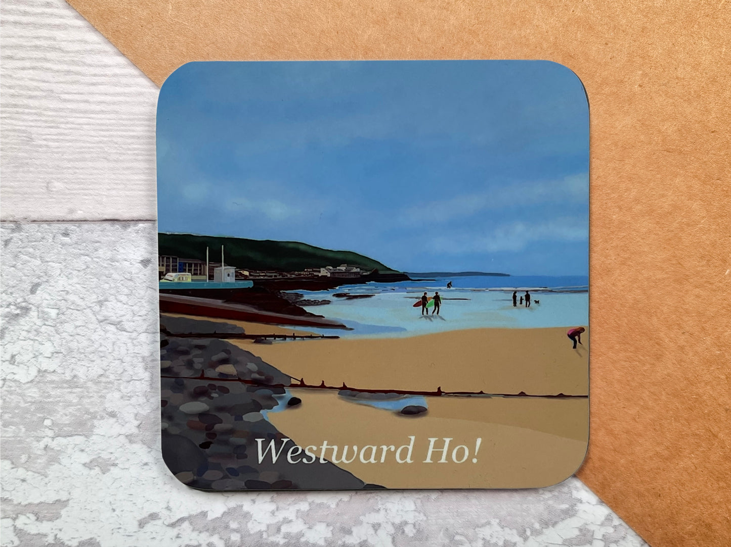 A table coaster featuring a print of Westward Ho Beach looking from the pebbleridge to the slipway with a Hockings Ice-Cream van and the cliffs in the distance