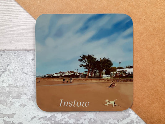 A table coaster featuring a print of Instow Beach in North Devon showing a small dog running on the beach, the Commodore Hotel and some large pine trees