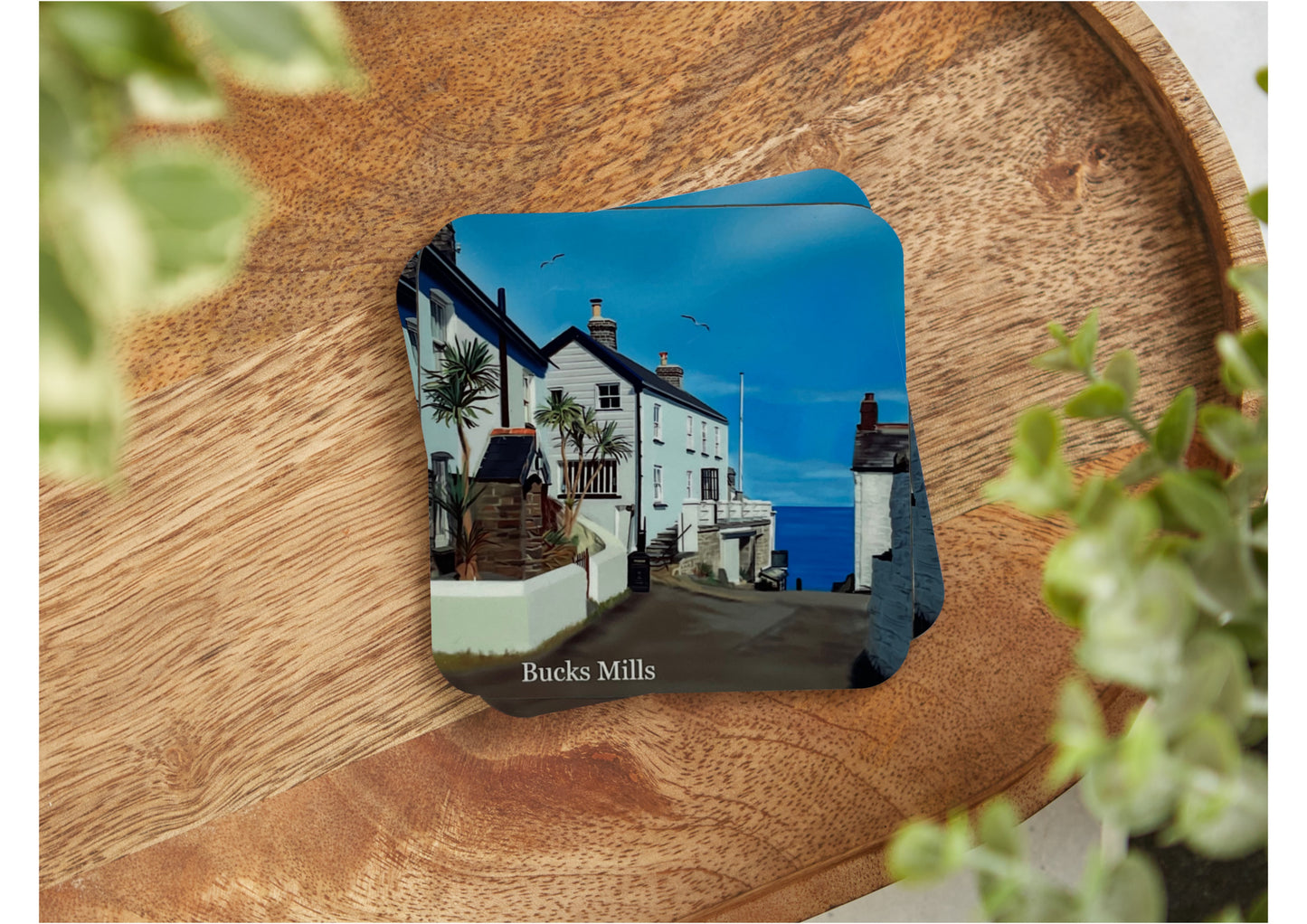 A table coaster handmade by Jagos Art featuring a print of Bucks Mills in North Devon showing the house at the top of the path leading to the sea and the sea in the distance