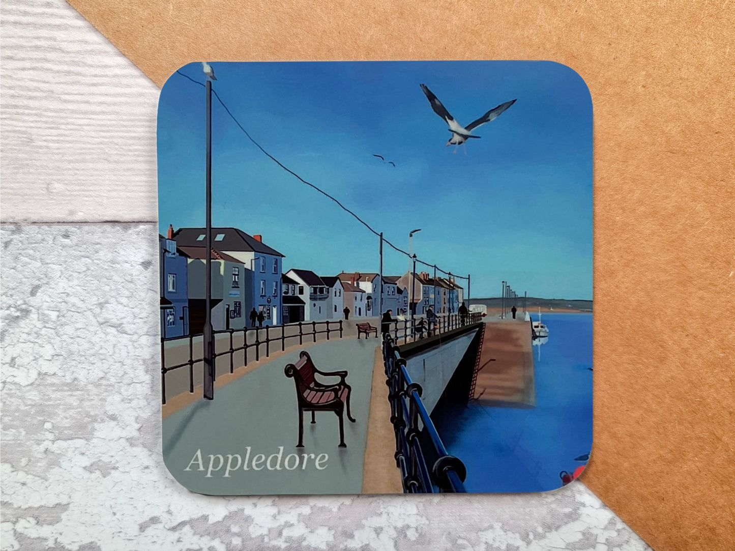 A table coaster handmade by Jagos Art featuring a print of a Appledore Quay in North Devon on a blue sky day