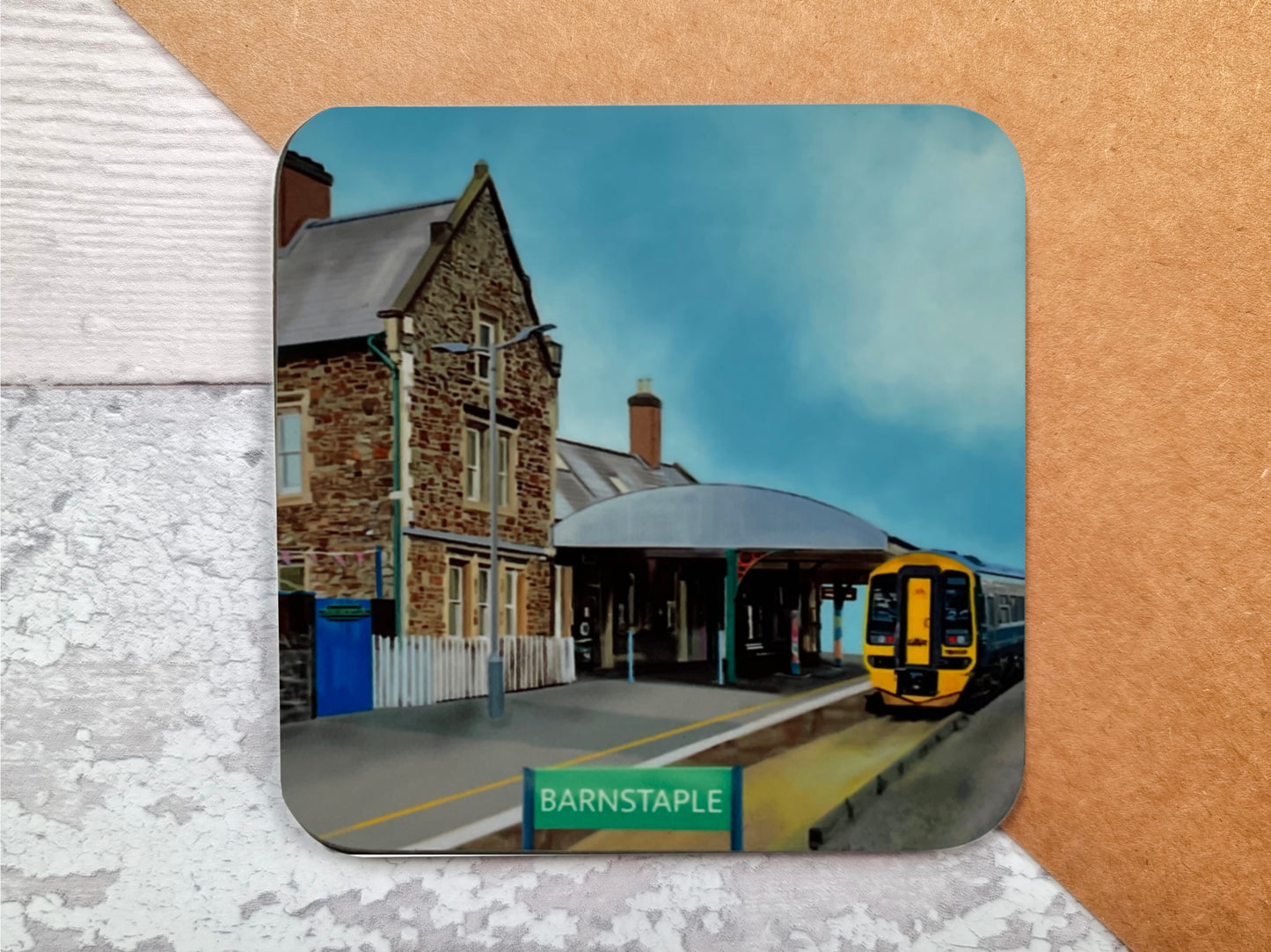 A table coaster handmade by Jagos Art featuring Barnstaple Train Station showing the Station Masters Cafe, the platform and the train arriving at the station