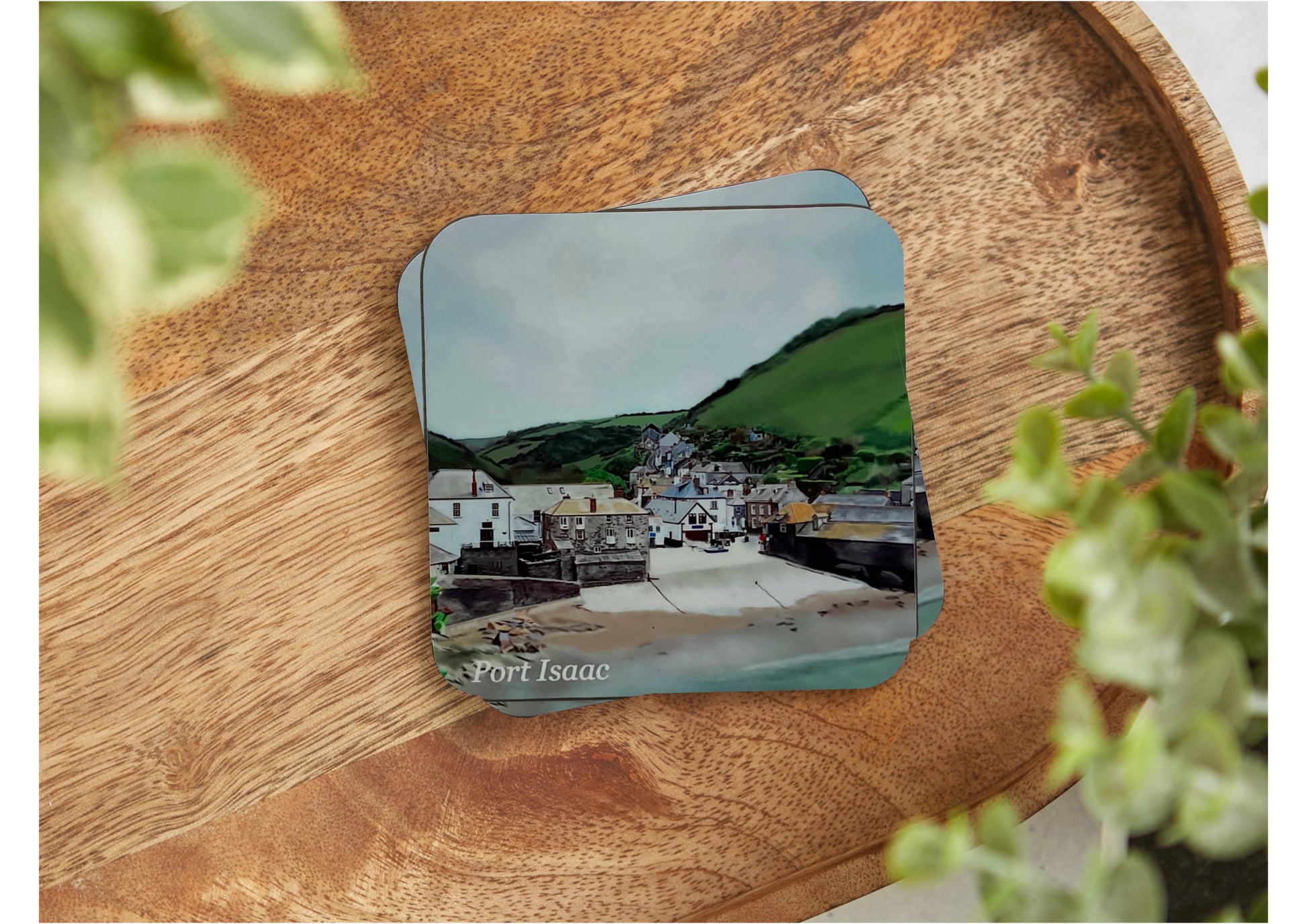 A table coaster featuring a print of Port Isaac in Cornwall showing the beach, the village and the fields in the background