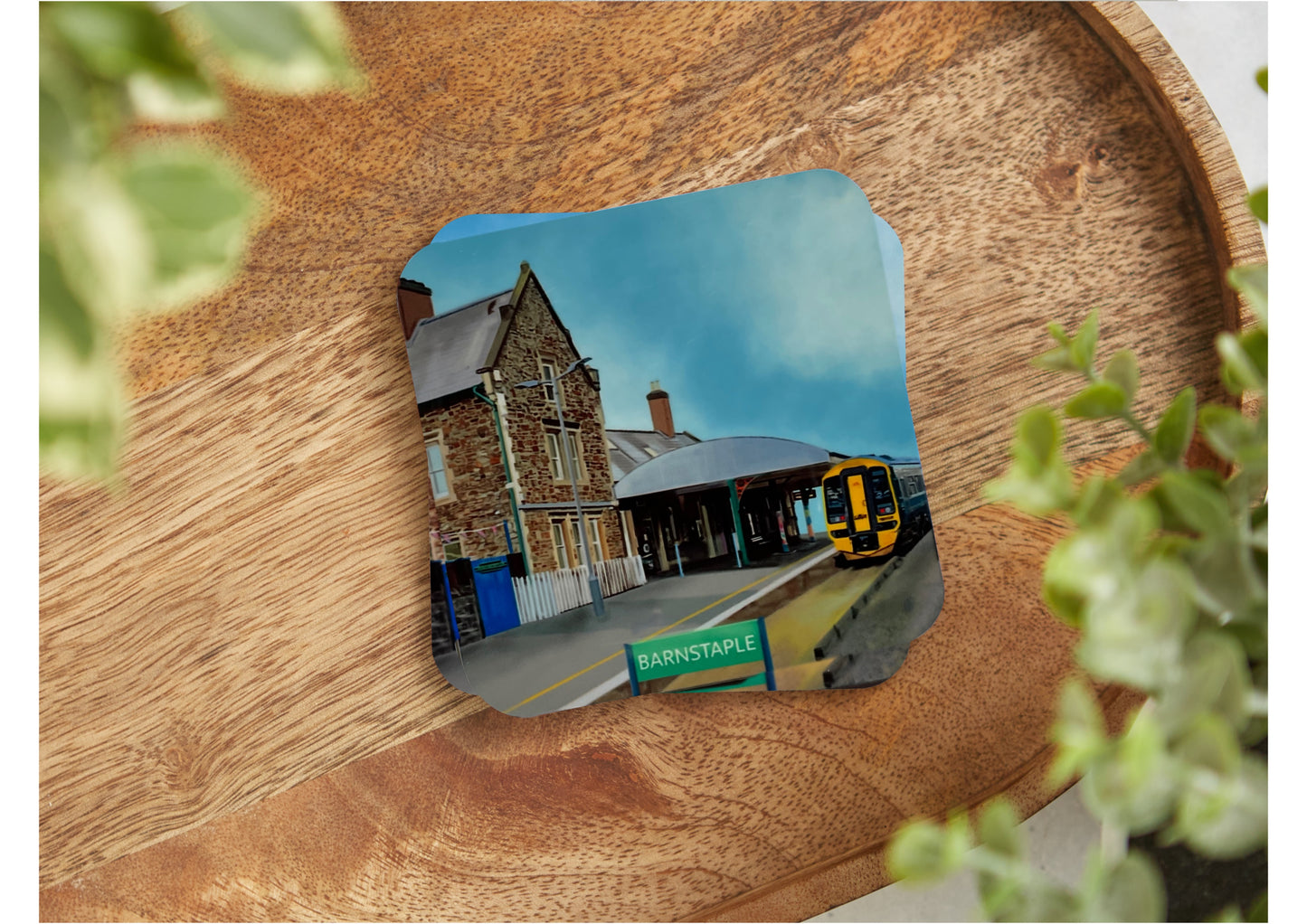 A table coaster handmade by Jagos Art featuring a print by Jagos Art of Barnstaple Train Station showing the Station Masters House, the platform and a train arriving at the station