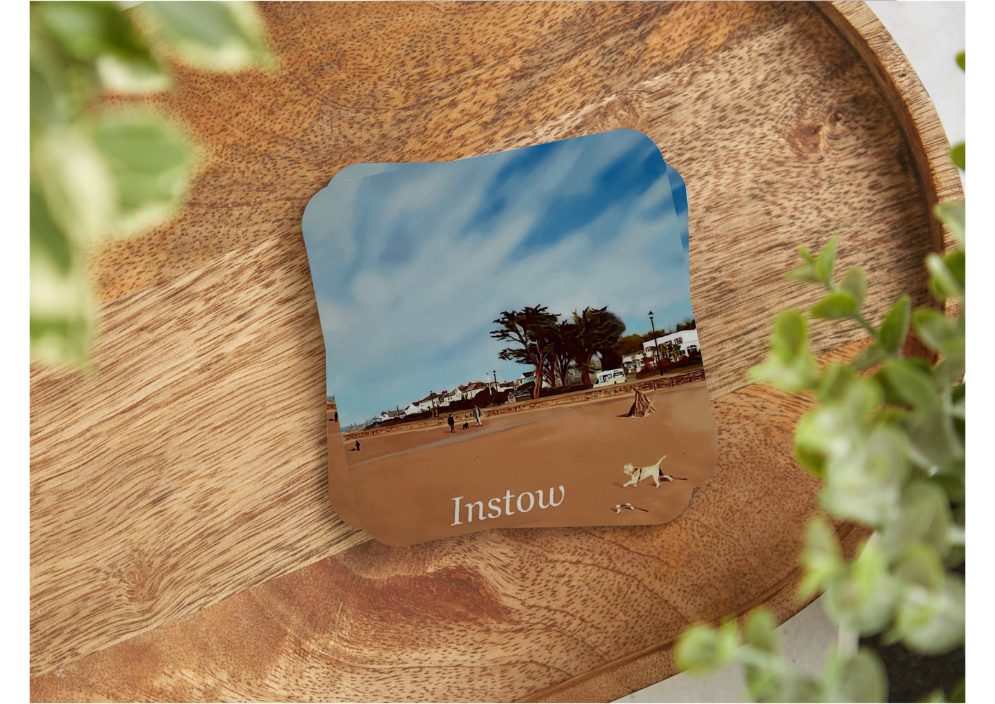 A table coaster featuring a print of Instow beach in North Devon showing the beach front with a small dog running, the Commodore Hotel, blue skies and some pine trees