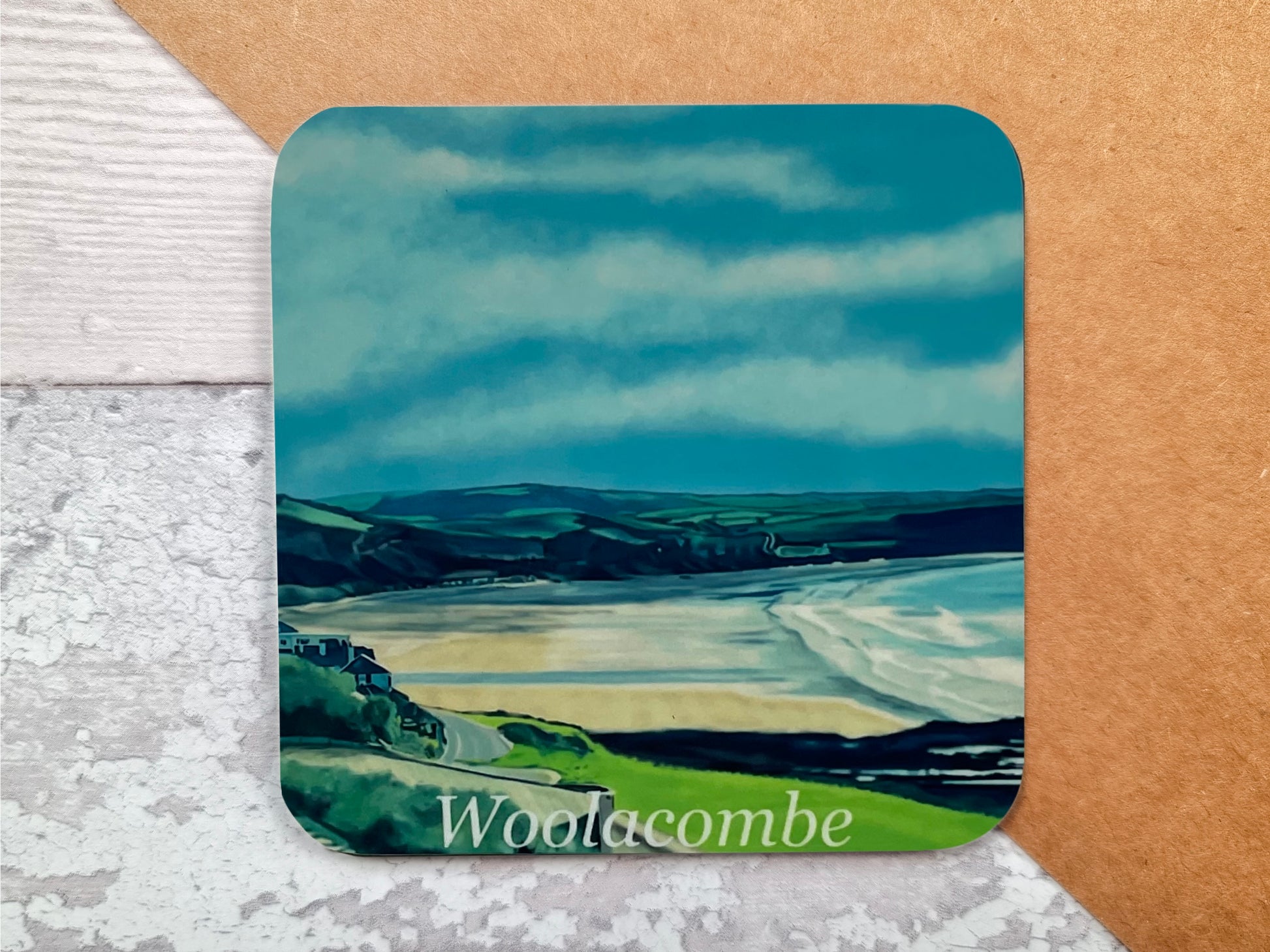 a table coaster featuring a print of Woolacombe in North Devon showing the beach from the road and the field landscape in the distance