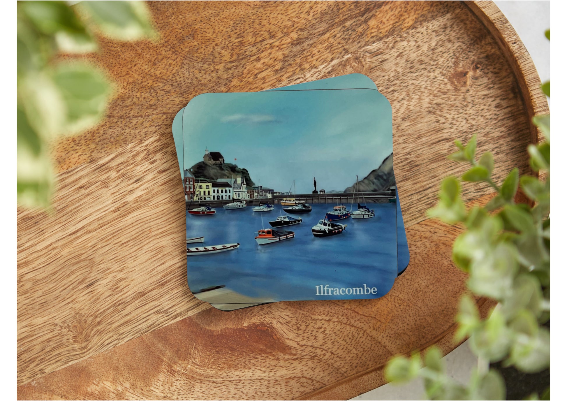 A table coaster featuring a print of Ilfracombe in North Devon showing the Harbour, several fishing boats, some buildings, verity in the distance and the church on the hill