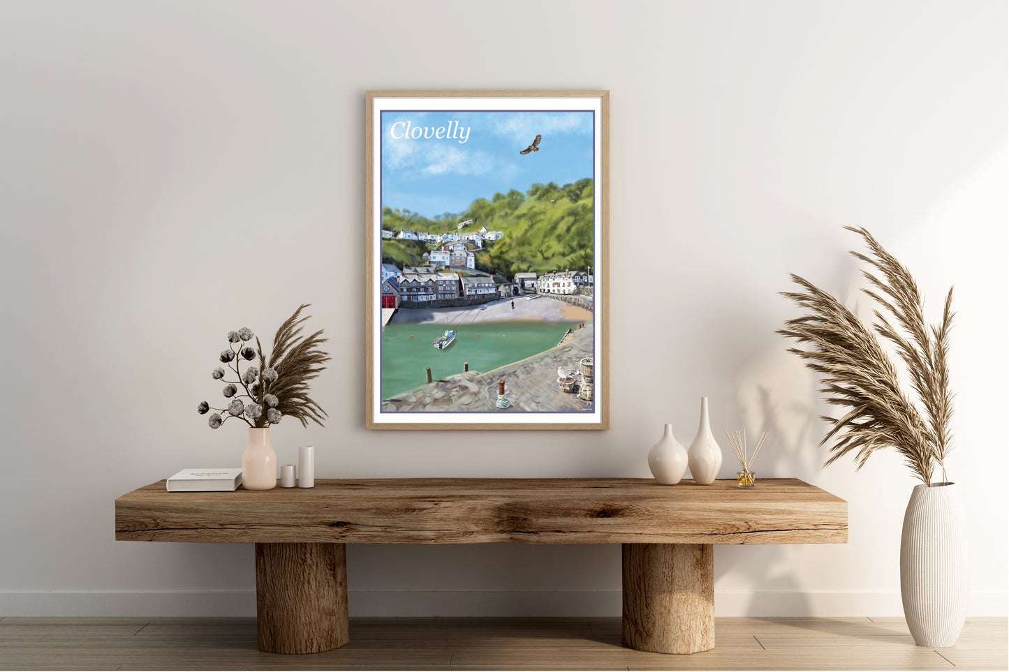 An art print by Jagos Art of the beautiful village of Clovelly in North Devon England showing the harbour with his quaint buildings, the red hotel and the lifeboat station, the small beach and a fishing boat moored with a buzzard flying overhead